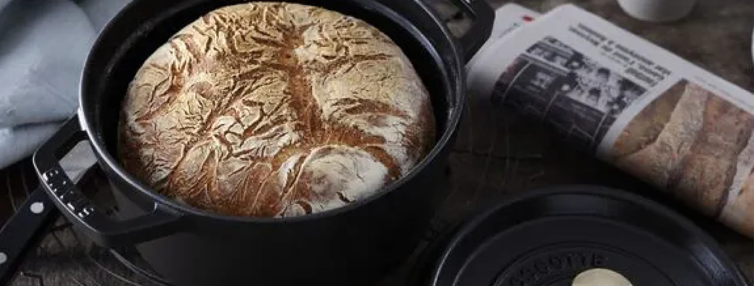 Staub Cocotte banner preta em contecto com pão dentro e jornal